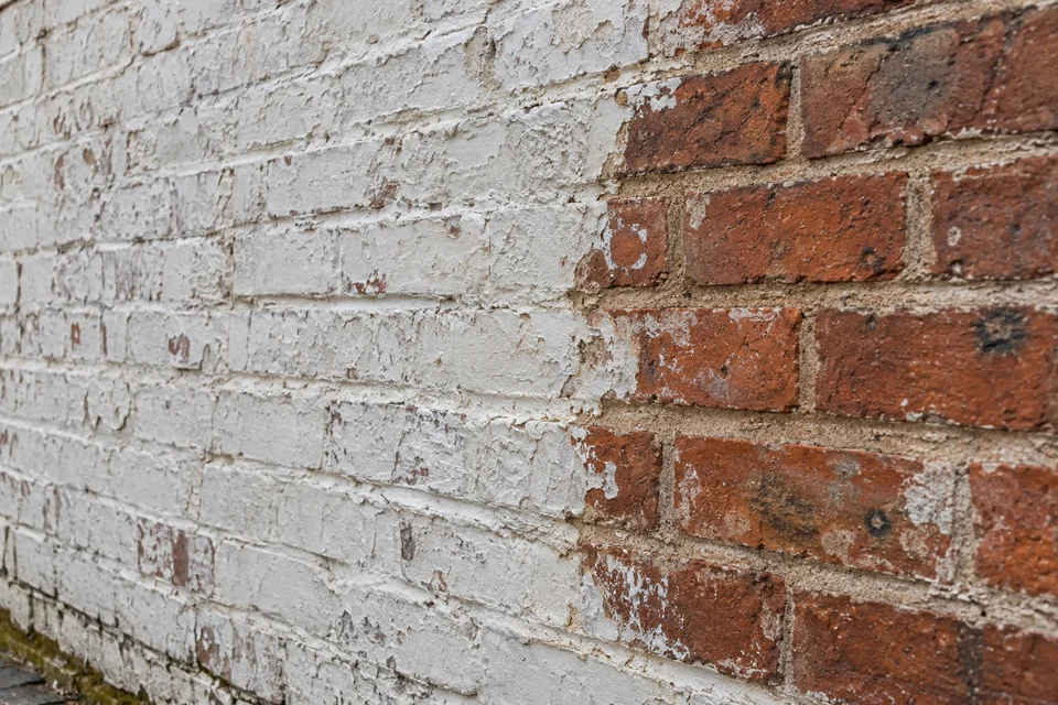 White paint on exterior brickwork beside a test patch revealing red masonry